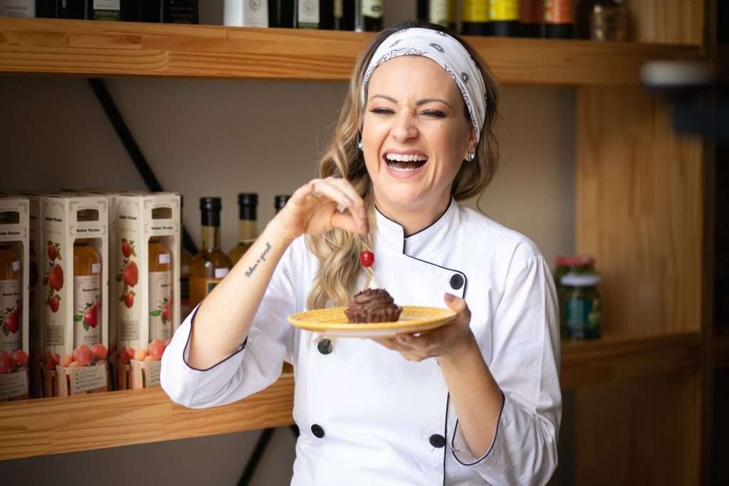Nathassia rindo enquanto coloca uma cereja em cima de um cupcake de chocolate em um prato