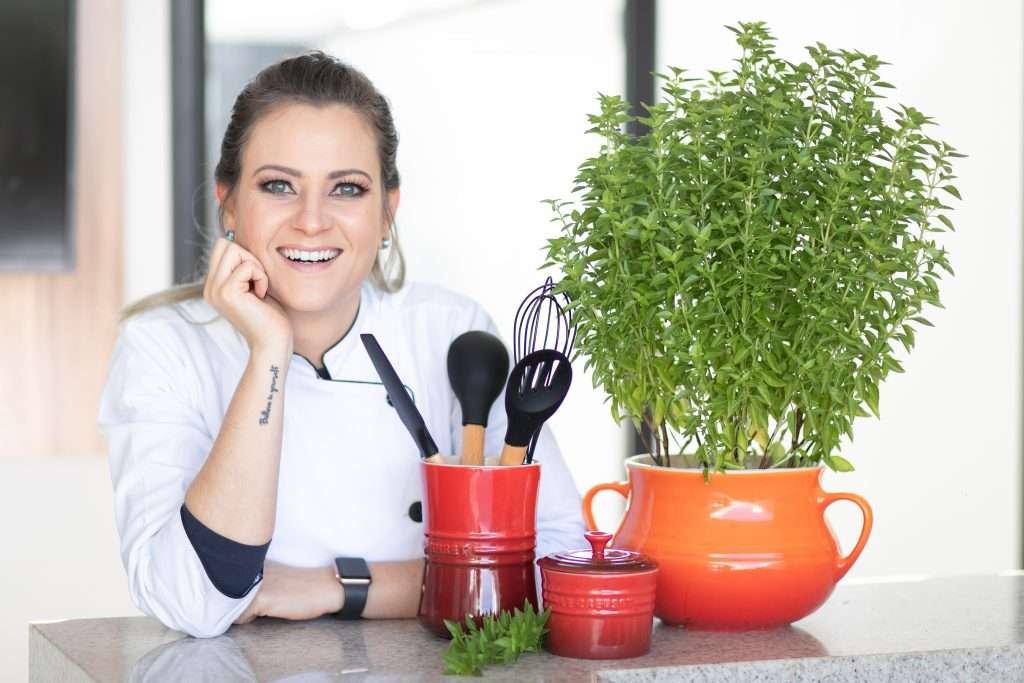 Nathassia sorrindo ao lado de utensílios de cozinha e ervas