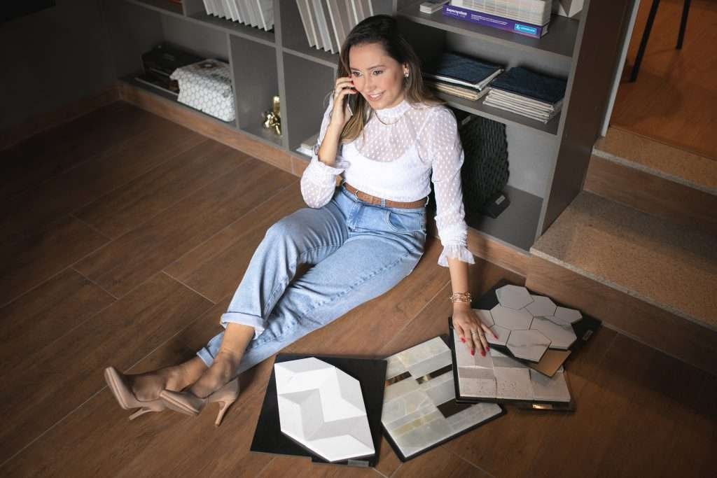 Rosi sentada no chão ao lado de uma estante de parede com amostras de ladrilhos no chão